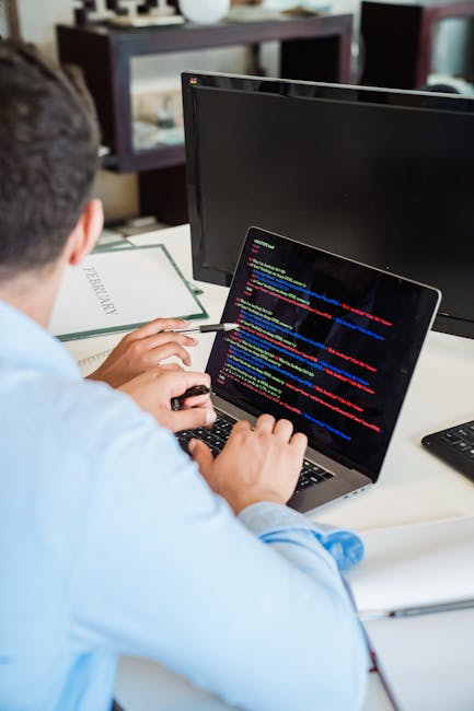 Close-up of a laptop screen displaying lines of code on the left side and a digital calculator interface with orange buttons on the right side, set on a desk in an office environment. The code include
